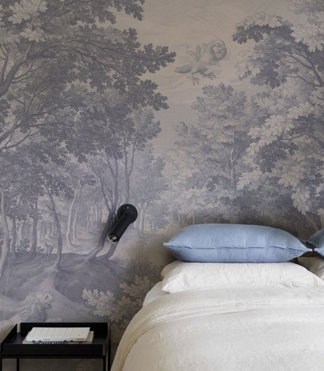 Blue patterned wallpaper with a forest scene behind a bed with white linens.